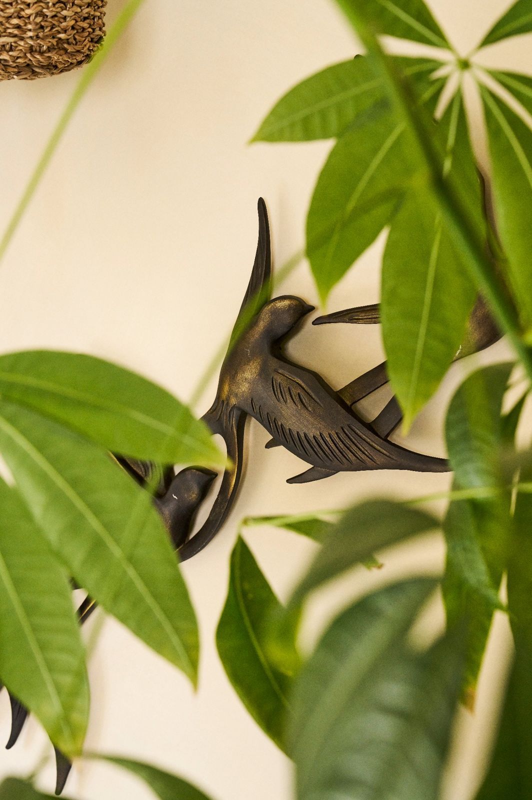 Bronze bird wall detail framed by soft green foliage.