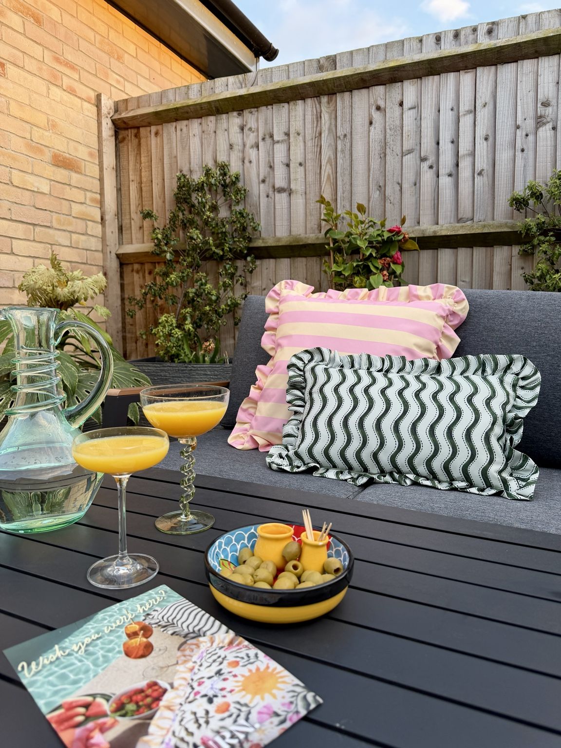 Outdoor seating with patterned cushions, drinks and styling — a relaxed garden sitting area.