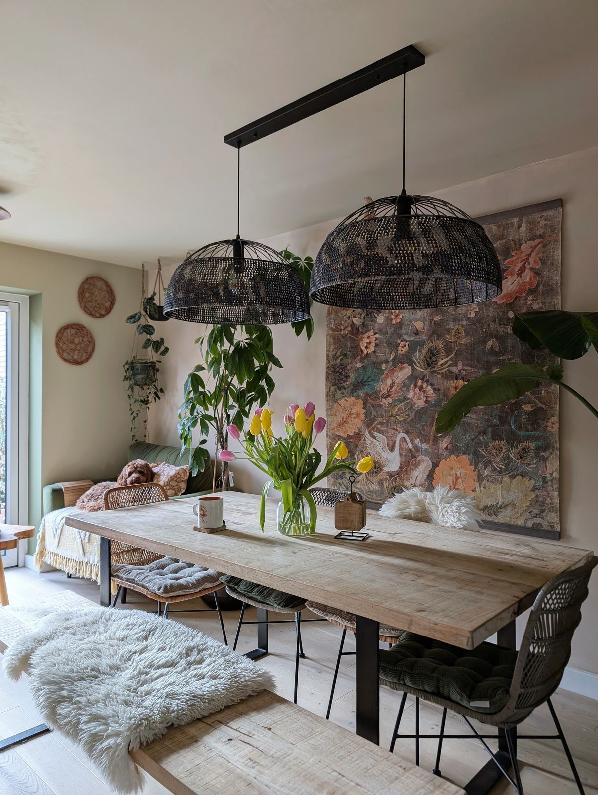 Dining nook at the heart of the home — wooden table, fresh tulips, hanging greenery and woven pendant lamps.