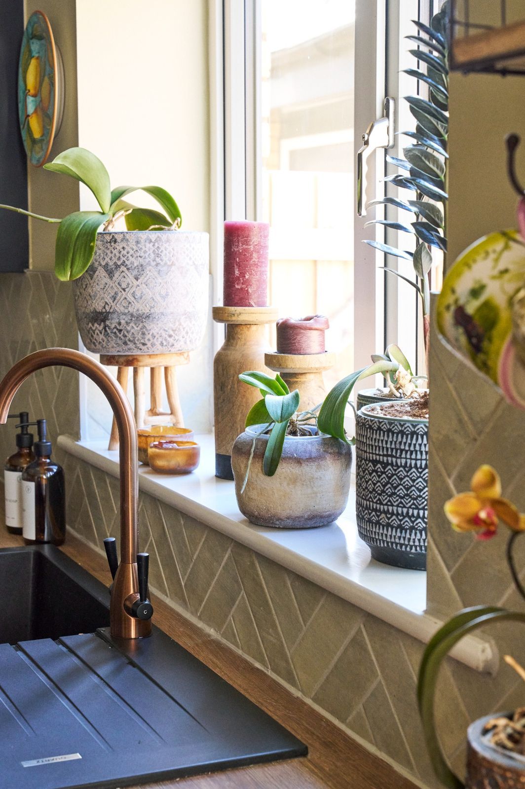 Kitchen window with potted plants, copper faucet and warm morning light.
